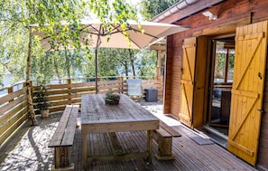 An outdoor wooden deck with a picnic table and benches, a wooden fence, and a building with a wooden door.