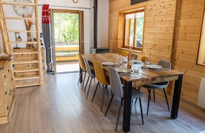 A wooden interior with a dining table set for four, a wooden cabinet with drawers, and a window with a view of greenery. - Chalet 'Des Sources, Avec Spa' with Mountain View, Private Terrace and Wi-Fi (Ramonchamp)