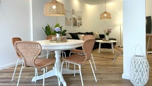 Un comedor con una mesa redonda, sillas blancas y lámparas colgantes de mimbre.