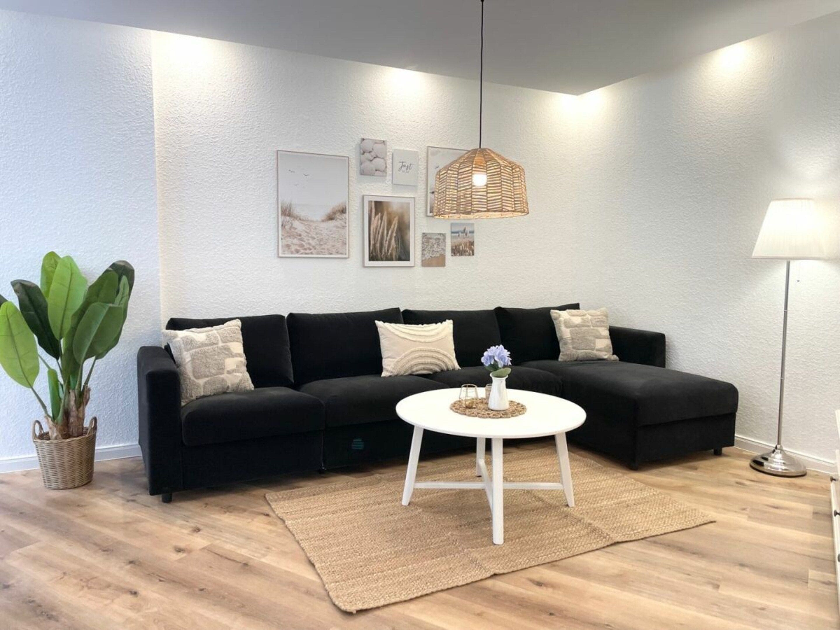 A modern living room with a black sofa, a round white coffee table, and a hanging wicker light fixture.