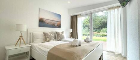 Quarto de hotel com cama, mesa de cabeceira, luminária, quadro e televisão.