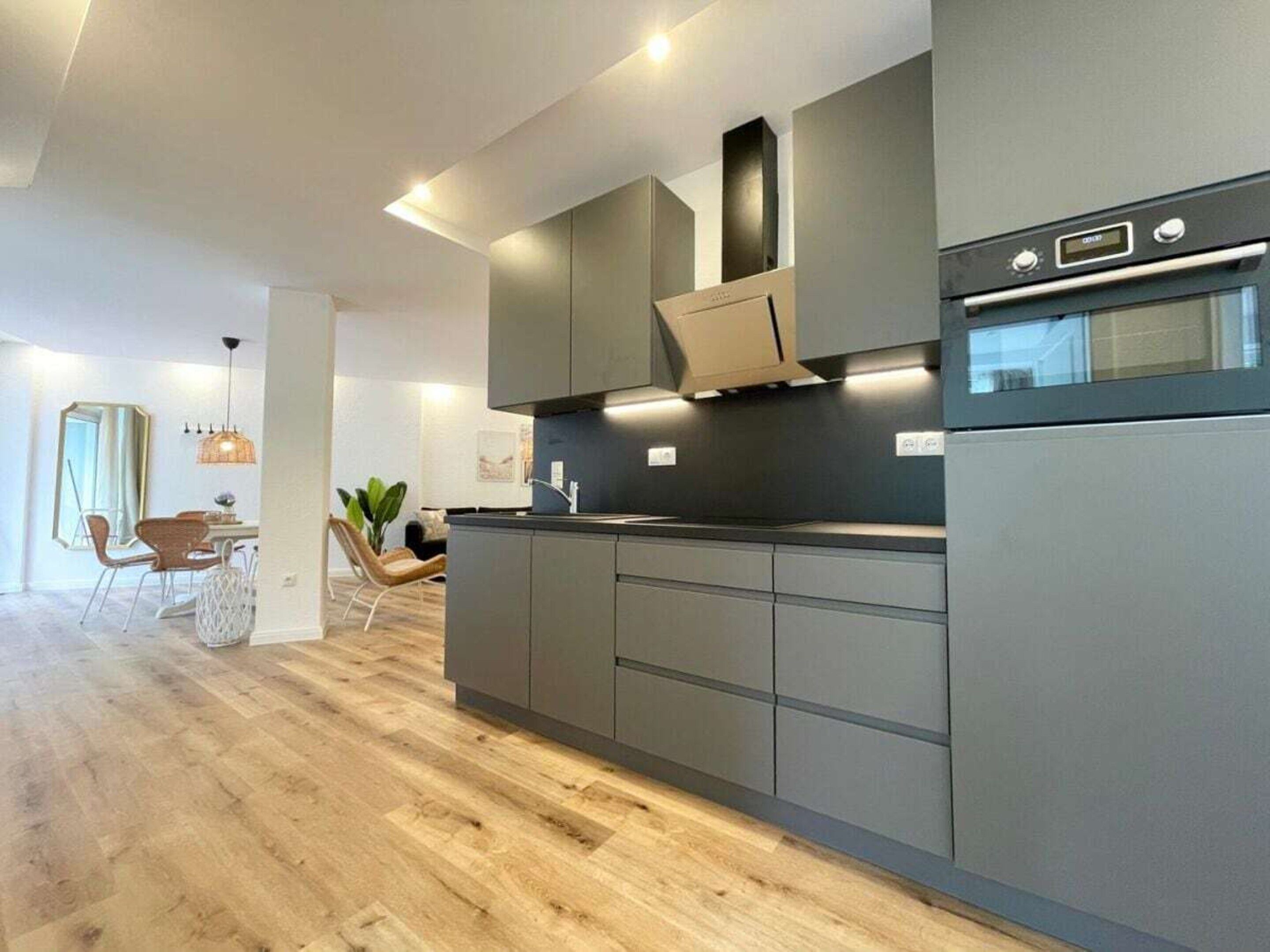 A modern kitchen with grey cabinetry, a built-in oven, and a dining area with a table and chairs.