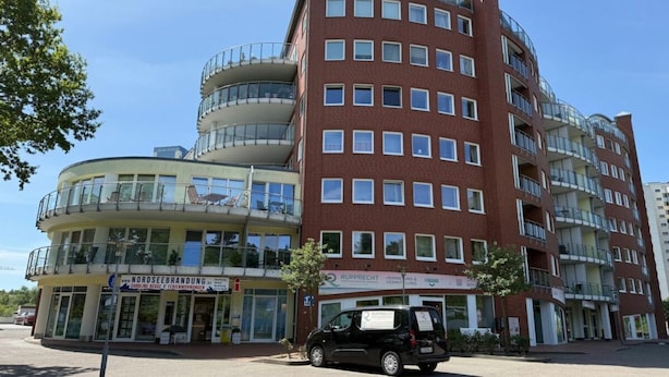 Un edificio de varios pisos con fachada curva, múltiples balcones y un espacio comercial en la planta baja.