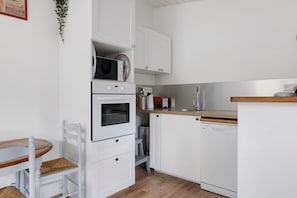Eine kleine Küche mit weißen Schränken, einer Mikrowelle, einem Backofen, einer Spüle und einem Geschirrspüler.