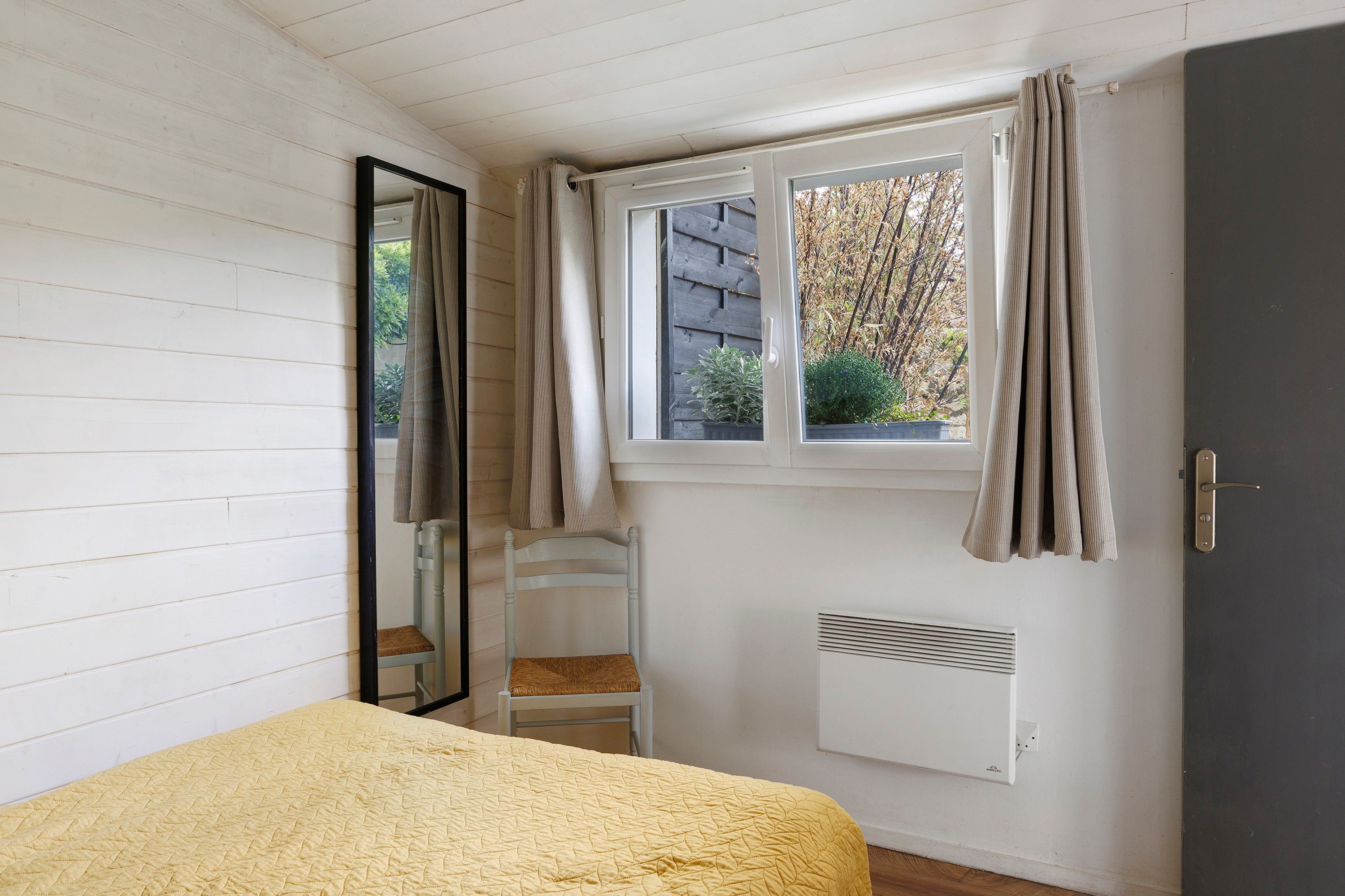 Une chambre à coucher avec un lit, une fenêtre avec des rideaux, un radiateur et une chaise.