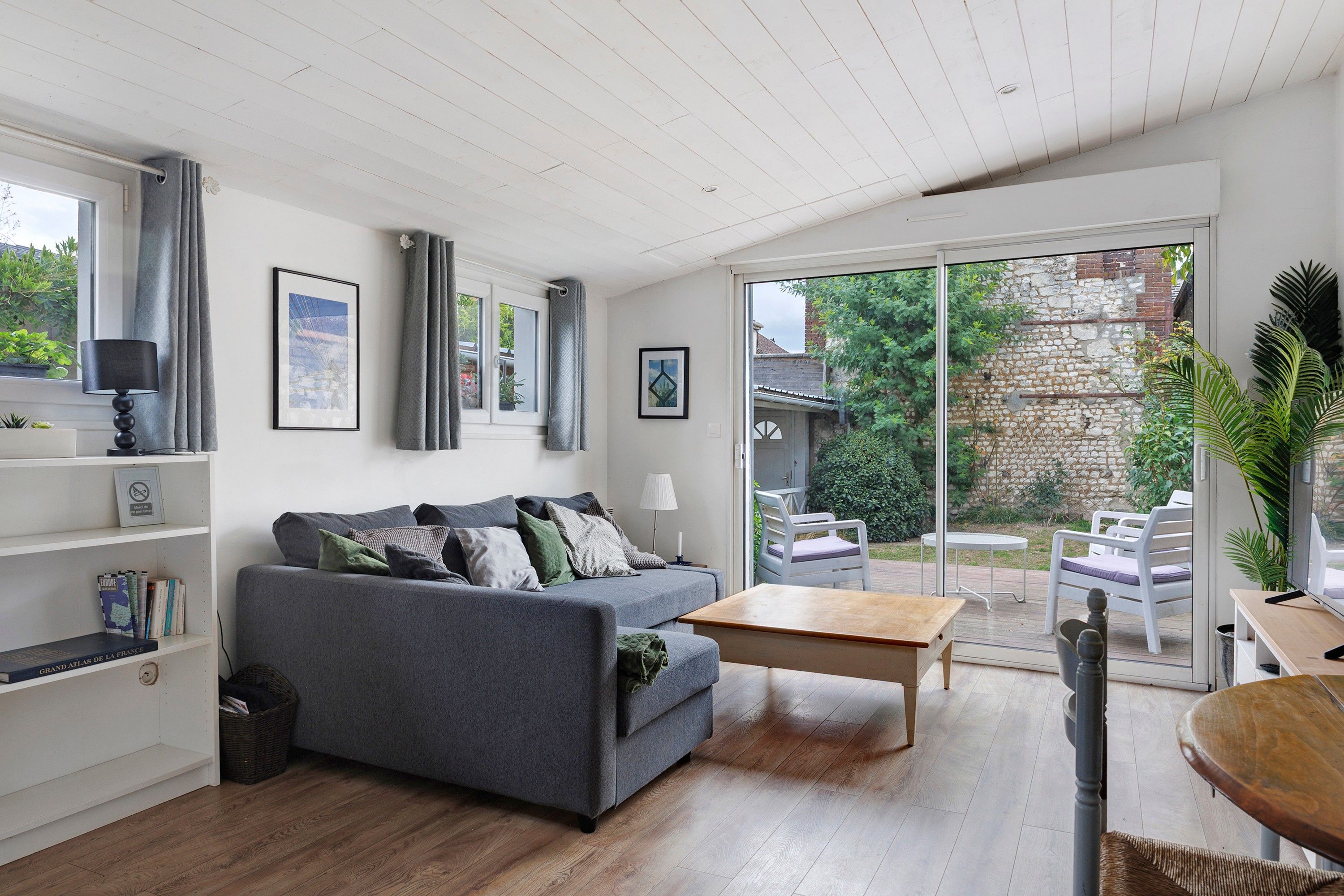 En moderne stue med en grå sofa, et træbord og en skydedør til en udendørs terrasse.