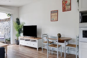 Ein Wohnzimmer mit Fernseher auf einem weißen Schrank, einem Esstisch mit Stühlen und einer Steinwand.