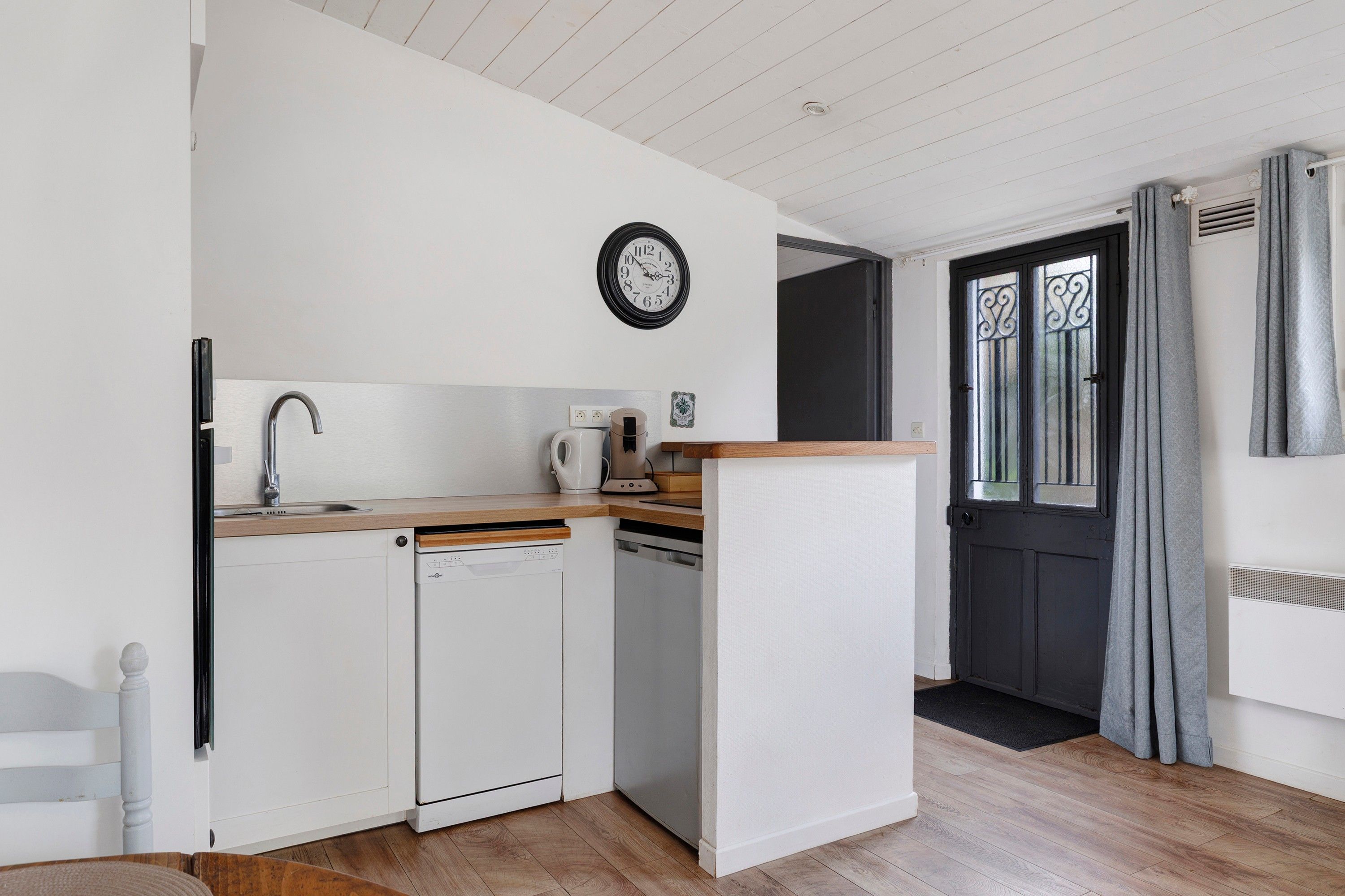 Cocina compacta con lavavajillas, cafetera y un reloj en la pared.