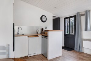 Cocina compacta con lavavajillas, cafetera y un reloj en la pared.