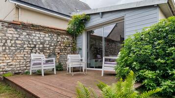 Un patio con dos sillas blancas, una terraza de madera y un muro de piedra.