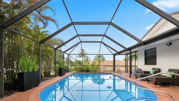 Una piscina interior con techo de vidrio, rodeada de palmeras y una terraza de madera.