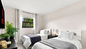 Habitación de hotel moderna con dos camas, un ventanal con vistas a zonas verdes, un televisor de pantalla plana y una mesita con una planta y un objeto decorativo.