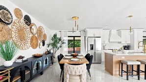 Una cocina moderna con armarios blancos, una isla central y una zona de comedor con mesa y sillas de madera.