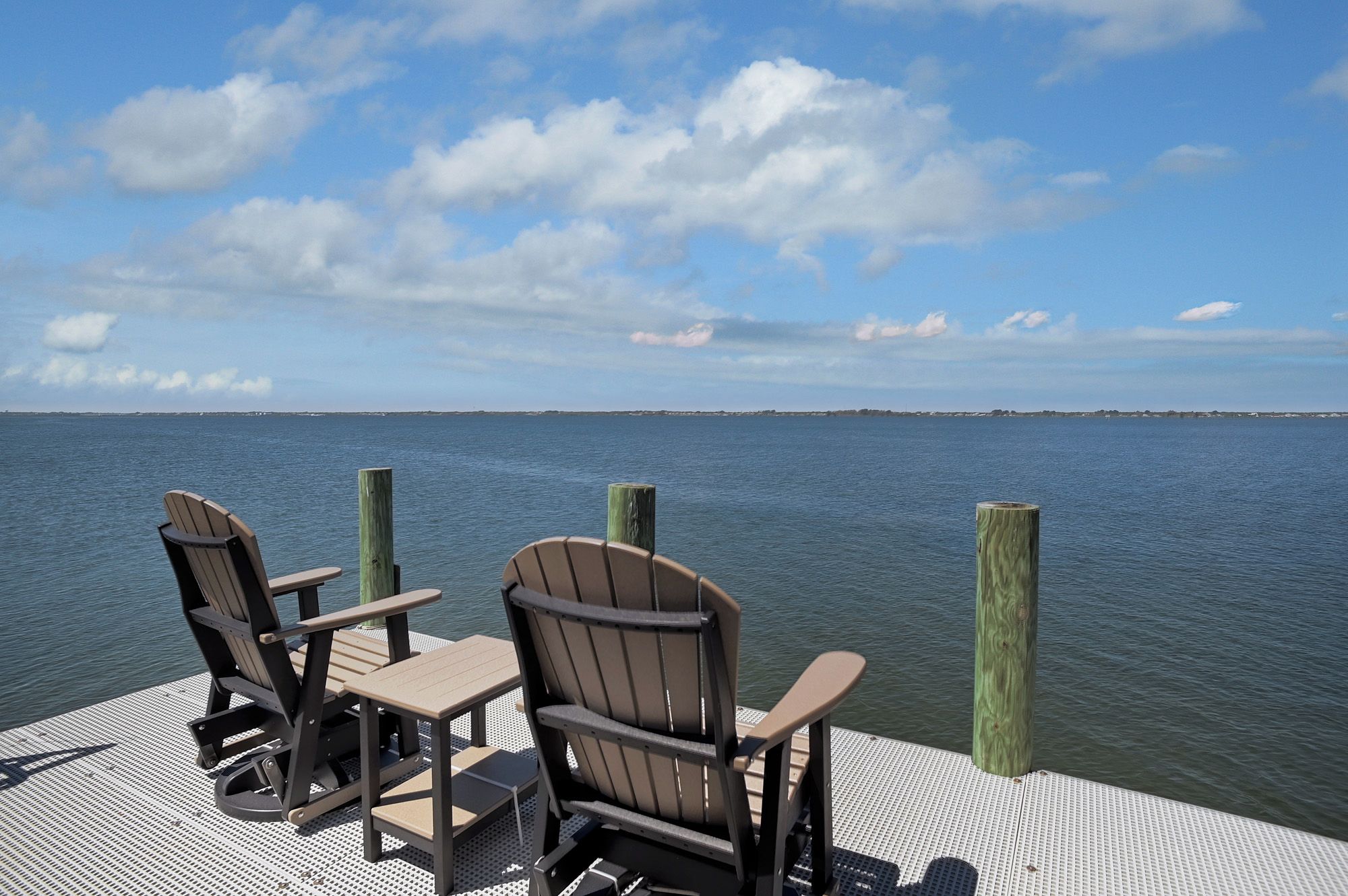 A deck with Adirondack chairs and a table overlooking a calm body of water.