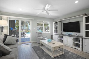 A living room with a sofa, a coffee table, a TV, and a ceiling fan. - Oasis Incredible River Front/Ocean Access w/Dock (Melbourne Beach)