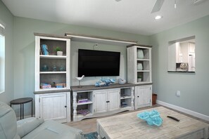 A living room with a TV, built-in shelves, a coffee table, and a sofa. - Oasis Incredible River Front/Ocean Access w/Dock (Melbourne Beach)