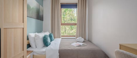 Un dormitorio con cama, escritorio, silla, ventana con cortinas y aire acondicionado.
