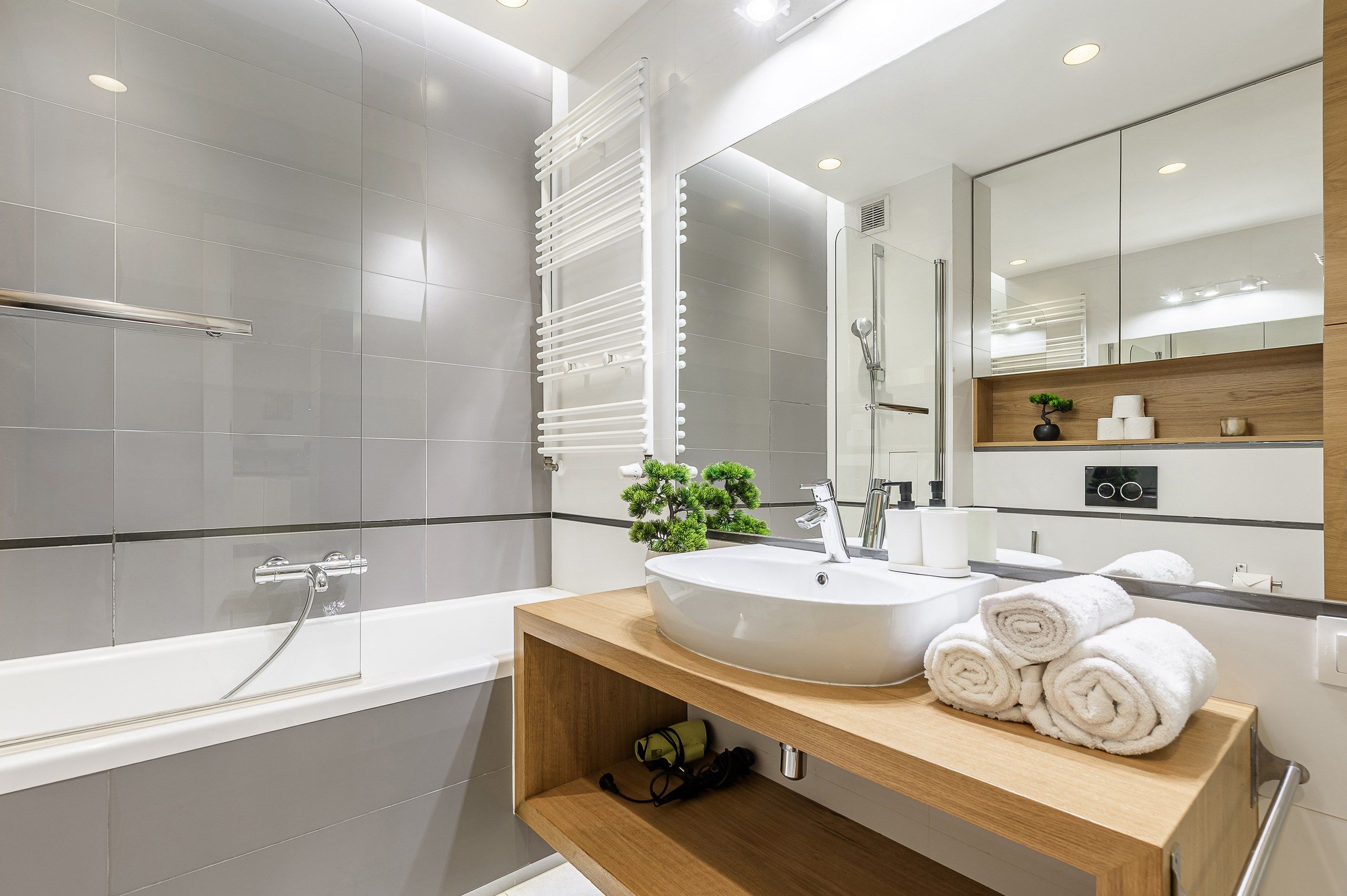 A modern bathroom with a bathtub, a sink with a mirror, and a wooden vanity.