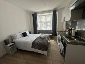 Et lille hotelværelse med seng, et lille natbord, vaskemaskine og tekøkken.