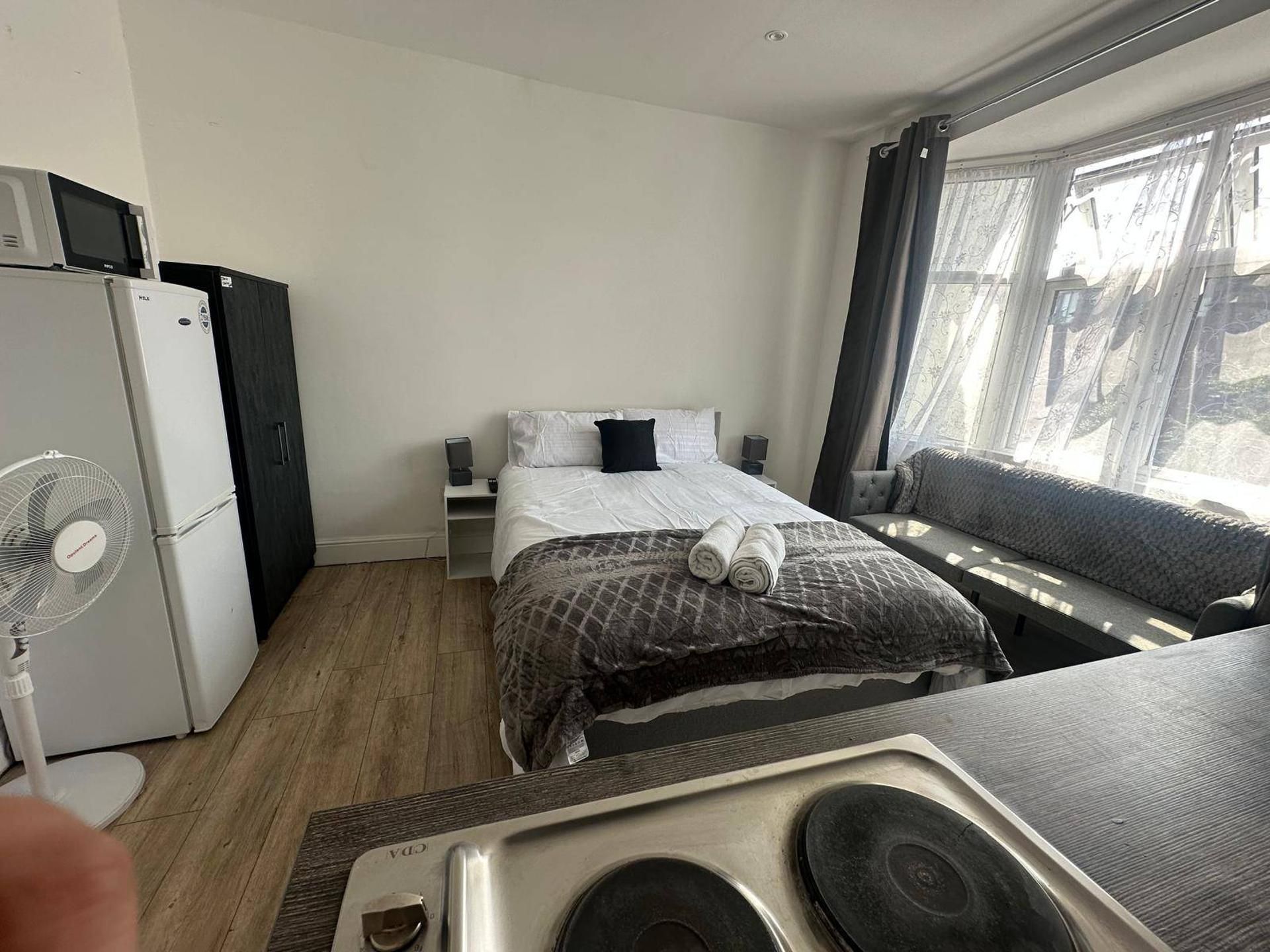 A hotel room with a bed, a small table, a chair, a fan, a heater, and a window with curtains.
