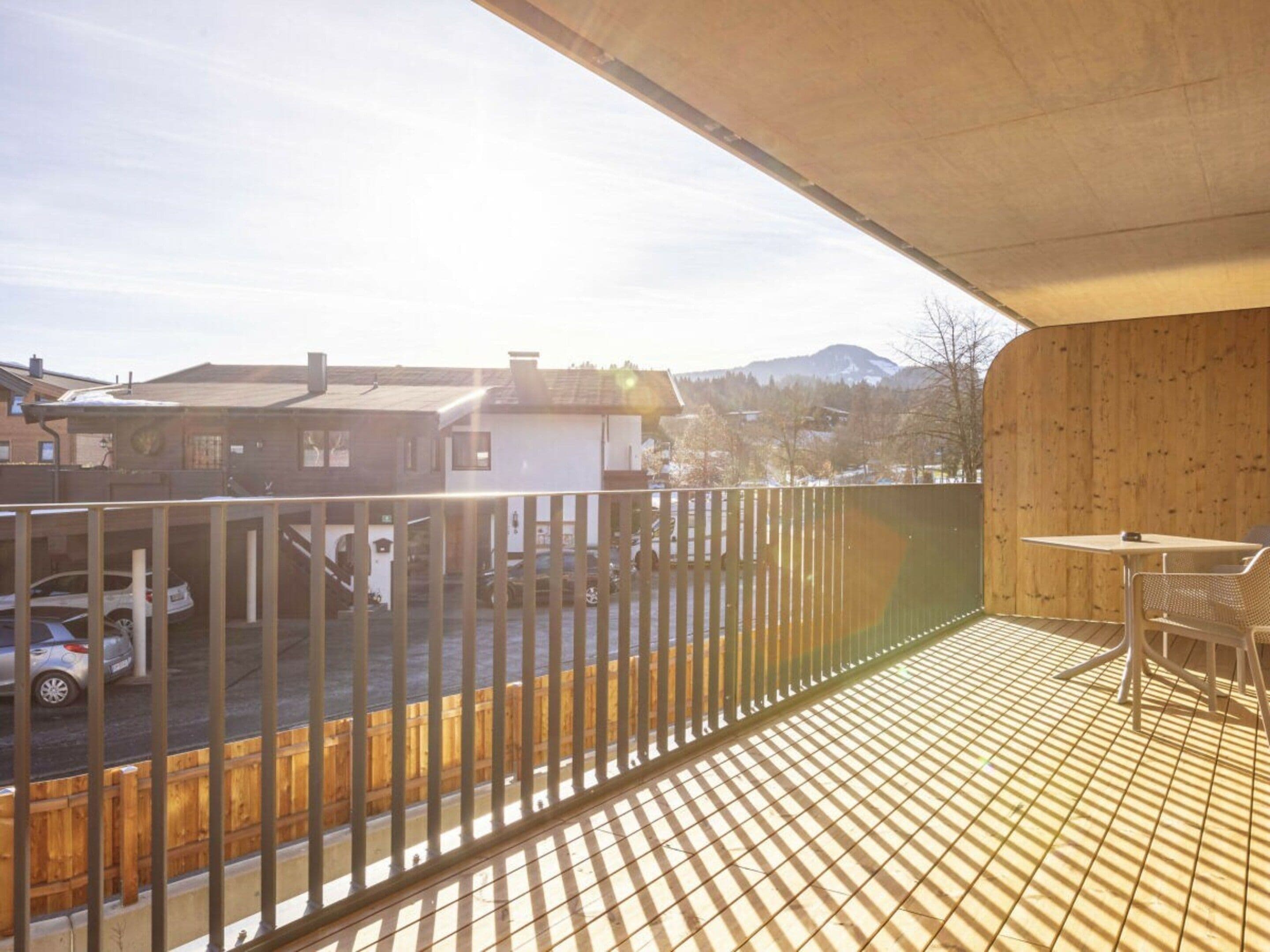 A balcony with a view of a parking area and houses, a table with chairs, and a wooden wall.