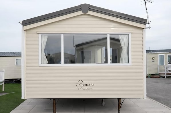 A mobile home with a pitched roof, large windows, and a 'Caemarfon' logo on the side. - Seaside Cabin Retreat in Towyn (Abergele)