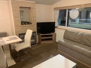 A living room with a television, a sofa, a dining table, and a chair. - Seaside Cabin Retreat in Towyn (Abergele)