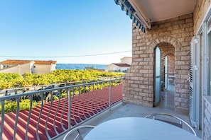 Ein Balkon mit rotem Dach, einer Steinsäule und Blick auf Weinberge.