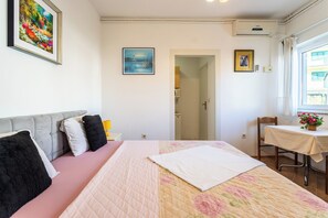 Ein Schlafzimmer mit einem Bett, einem Nachttisch, einem Stuhl, einem Fenster und einer Tür zu einem anderen Raum.
