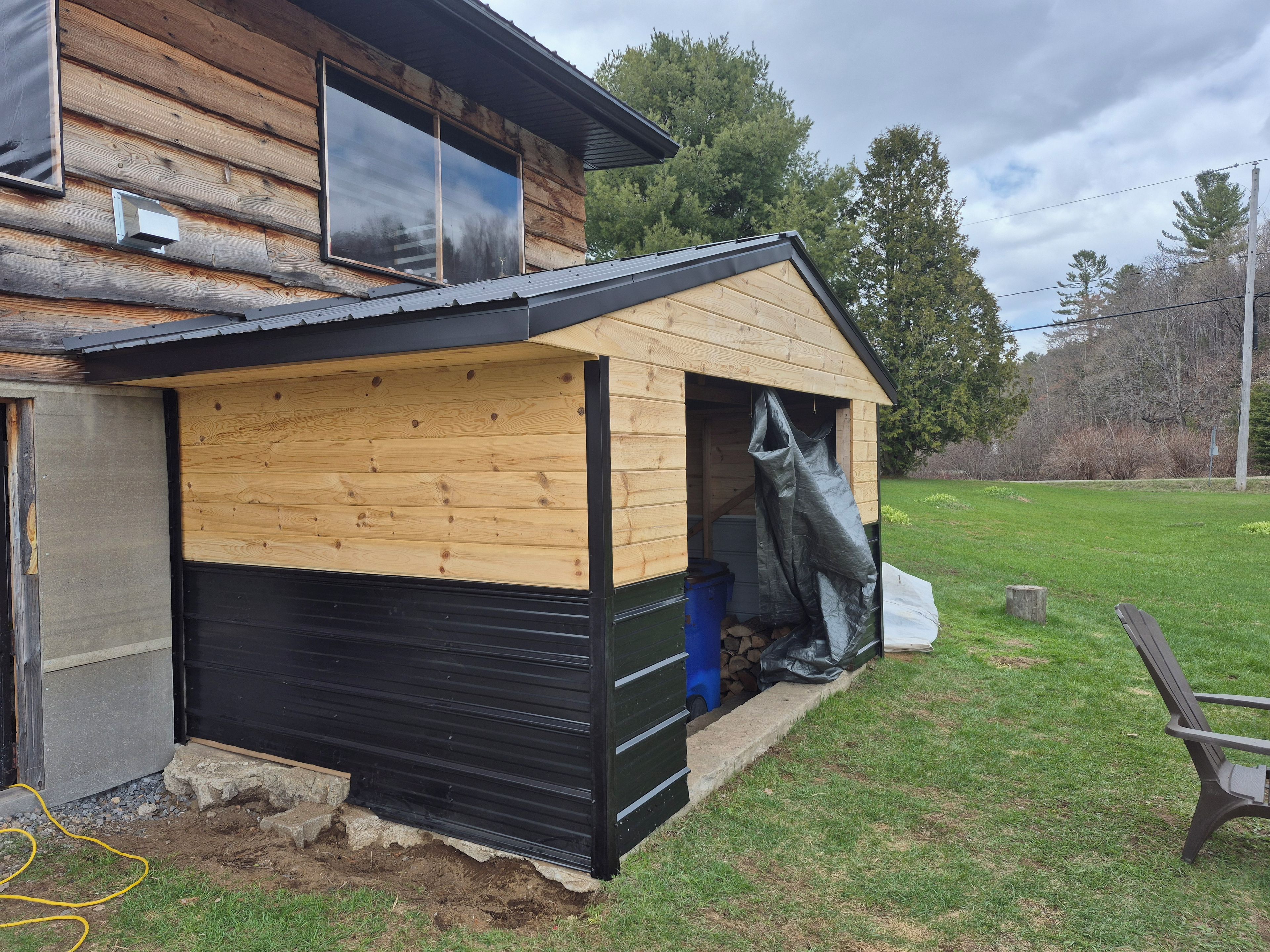 A wooden cabin with a black garage door, a covered porch, and a yard with a bench.