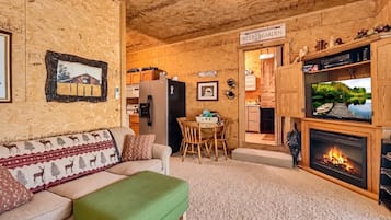 Ein gemütliches Wohnzimmer mit Kamin, einem Essbereich und einer durch einen offenen Durchgang einsehbaren Küche.