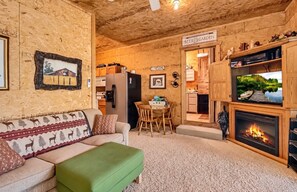 A cozy living room with a fireplace, a dining area, and a kitchen visible through an open doorway.