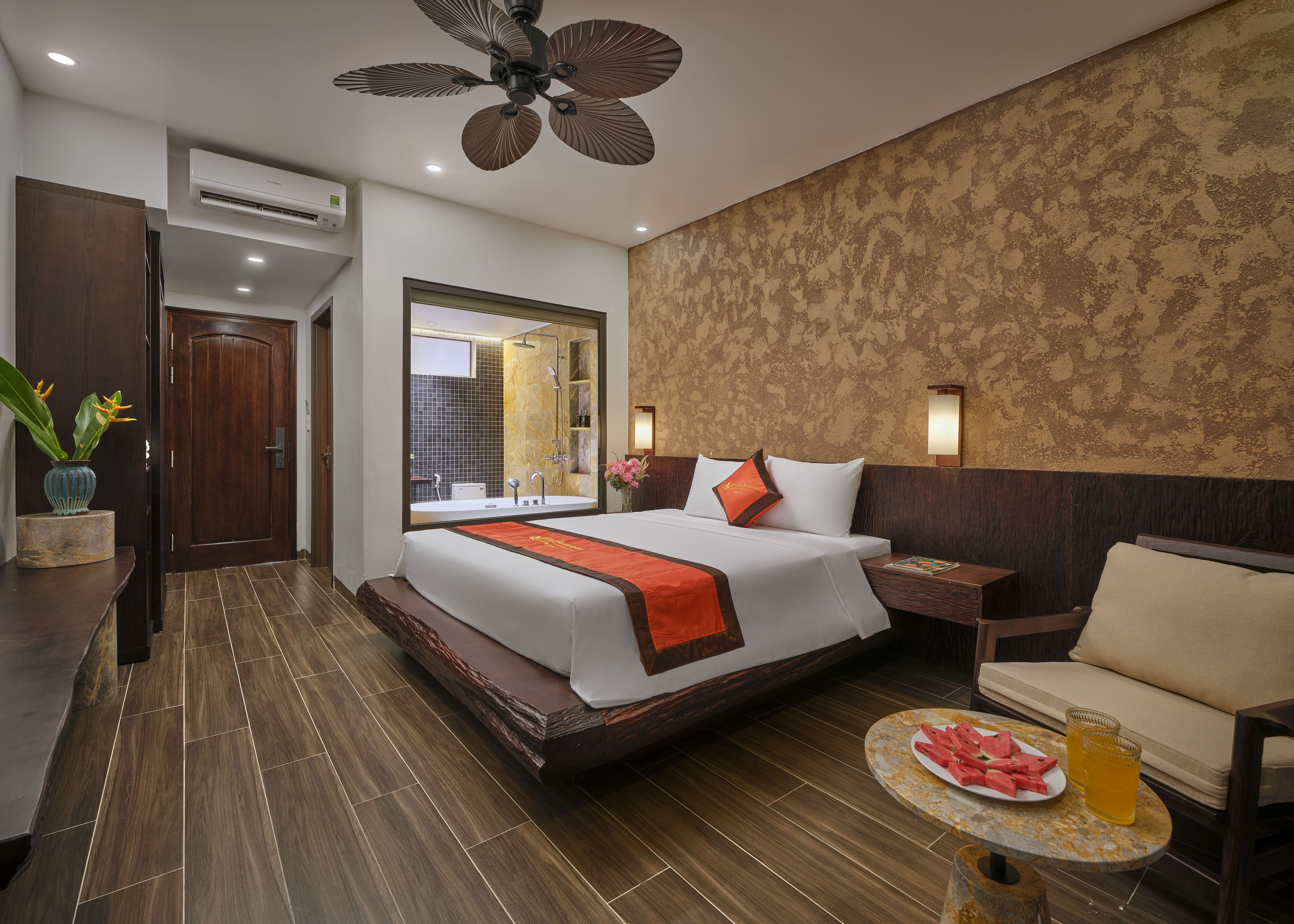 Ein Hotelzimmer mit einem großen Bett, einer Sitzecke mit Tisch, einer Duschkabine und einem Deckenventilator.