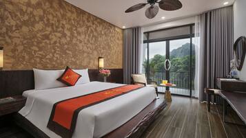 A hotel room with a large bed, a desk, a chair, a balcony with a view, and a ceiling fan.