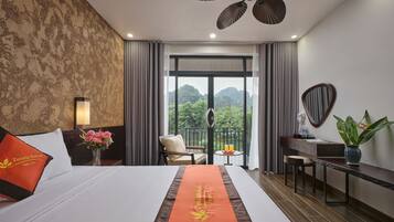 Ein Hotelzimmer mit einem großen Bett, einem Schreibtisch, einem Stuhl, einem Balkon mit Bergblick und einem Deckenventilator.
