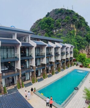 A hotel with multiple floors, a swimming pool, and a mountainous backdrop. - Zenvia Retreat Tam Coc (Nam Hoa Lư)