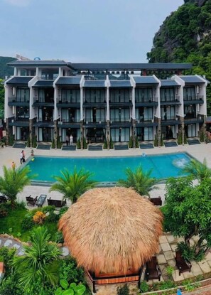 A multi-story hotel with a swimming pool and a thatched-roof structure in the foreground. - Zenvia Retreat Tam Coc (Nam Hoa Lư)