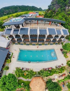 A hotel with a swimming pool, multiple balconies, and a view of the surrounding landscape. - Zenvia Retreat Tam Coc (Nam Hoa Lư)