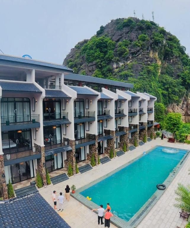 A hotel with multiple floors, a swimming pool, and a mountainous backdrop.