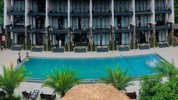 Ein mehrstöckiges Hotel mit Schwimmbad und einem Gebäude mit Strohdach im Vordergrund.
