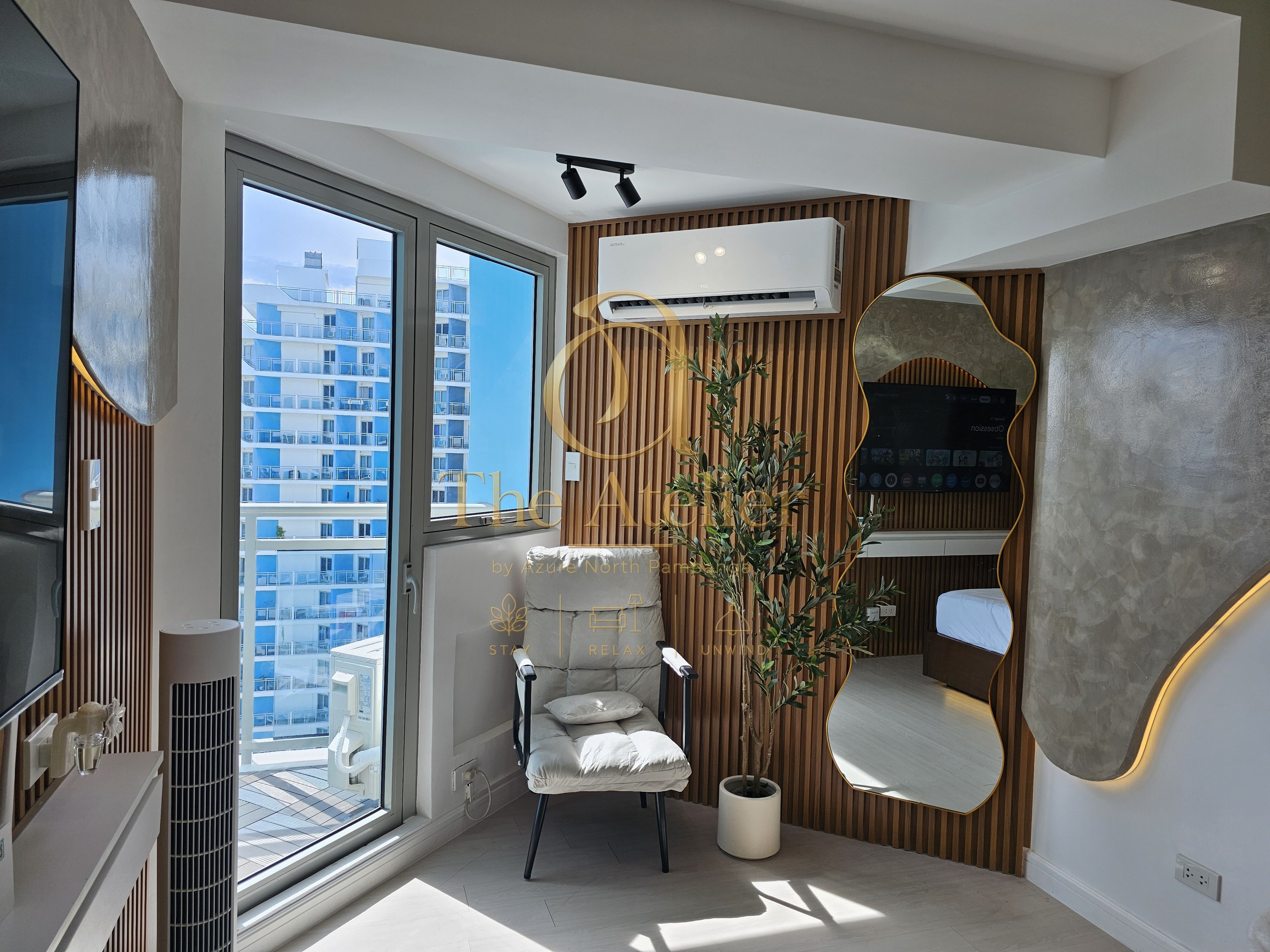A modern living room with a large window, a comfortable chair, a potted plant, and a wall-mounted air conditioning unit.