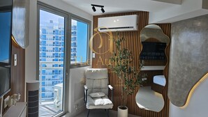 Un salon moderne doté d’une grande fenêtre, d’un fauteuil confortable, d’une plante en pot et d’un climatiseur fixé au mur.
