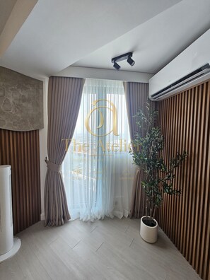 A modern room with a large window, a potted plant, and a ceiling-mounted air conditioning unit. - Atelier Azure North | Beach & Wave Pool (San Fernando)