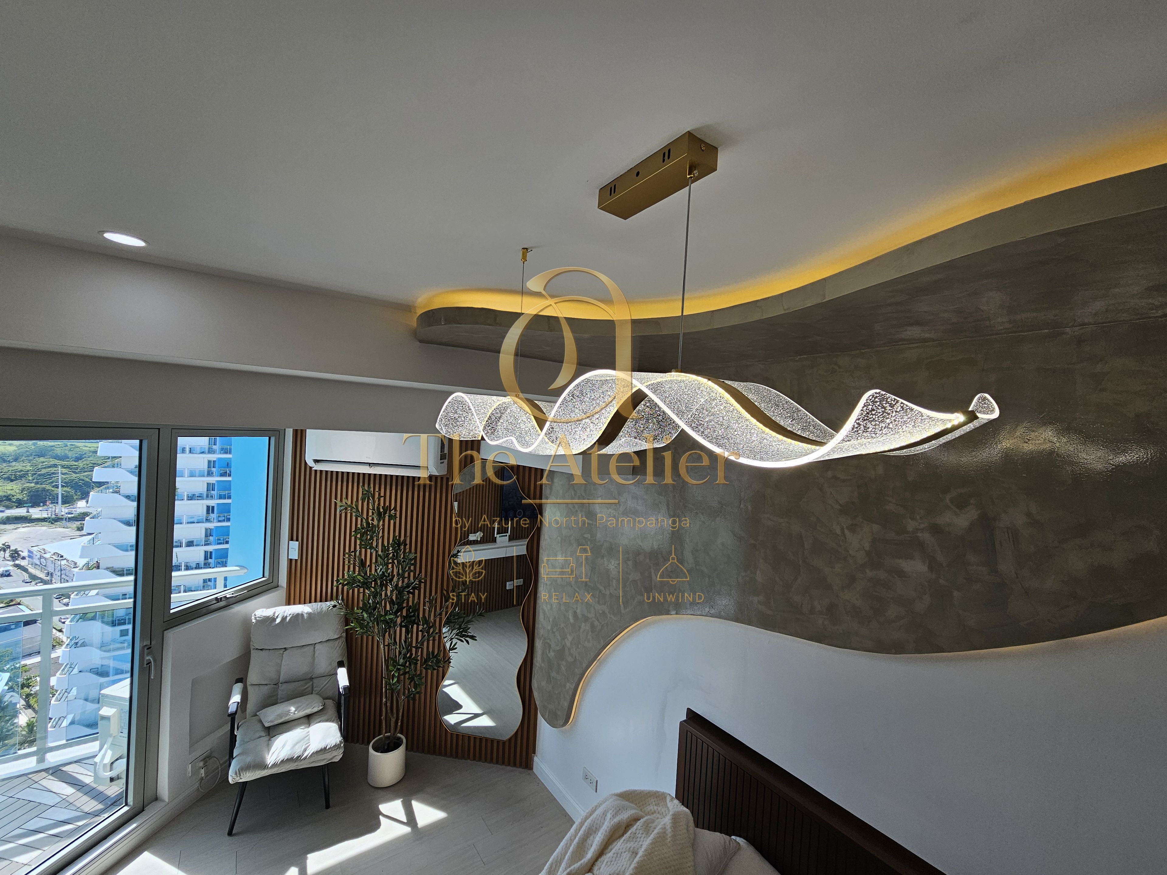 Une chambre d’hôtel moderne dotée d’une grande fenêtre, d’un mur aux lignes courbes et d’un luminaire original.