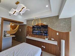 A modern hotel room with a bed, a vanity with a mirror, a wall-mounted TV, and a unique ceiling light fixture.