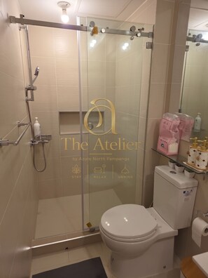 A modern bathroom with a glass shower enclosure, a toilet, and a sink with a glass shelf. - Atelier Azure North | Beach & Wave Pool (San Fernando)