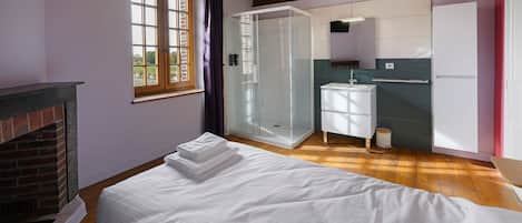 Ein Schlafzimmer mit Bett, Kamin, Dusche und einem Badezimmer inklusive Waschbecken und Spiegel.
