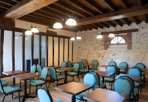 Ein Restaurantinnenraum mit Holzbalken, Steinwänden und mehreren Tischen und Stühlen.
