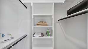 Un placard blanc avec des étagères où sont rangées des serviettes pliées et un fer à repasser.