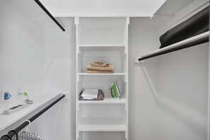 Ein weißer Kleiderschrank mit Regalen, gefüllt mit gefalteten Handtüchern und einem Bügeleisen.